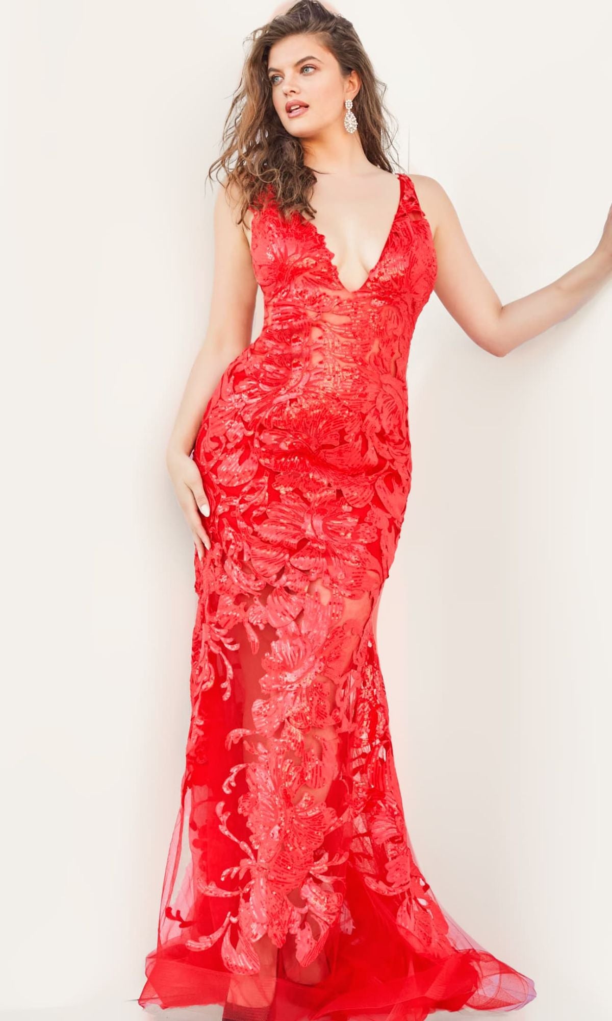 A woman poses in a fitted, sleeveless Jovani Plus-Size Sheer Prom Dress with sequins and a deep V-neck, against a plain light background.
